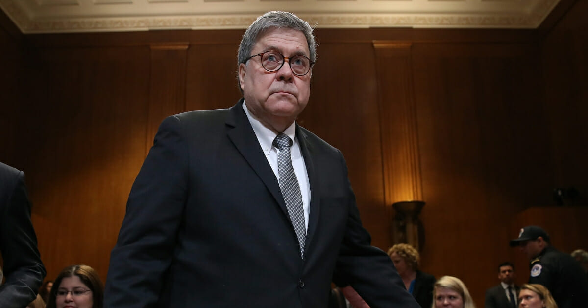 Barr standing with his hand resting on the back of a chair.
