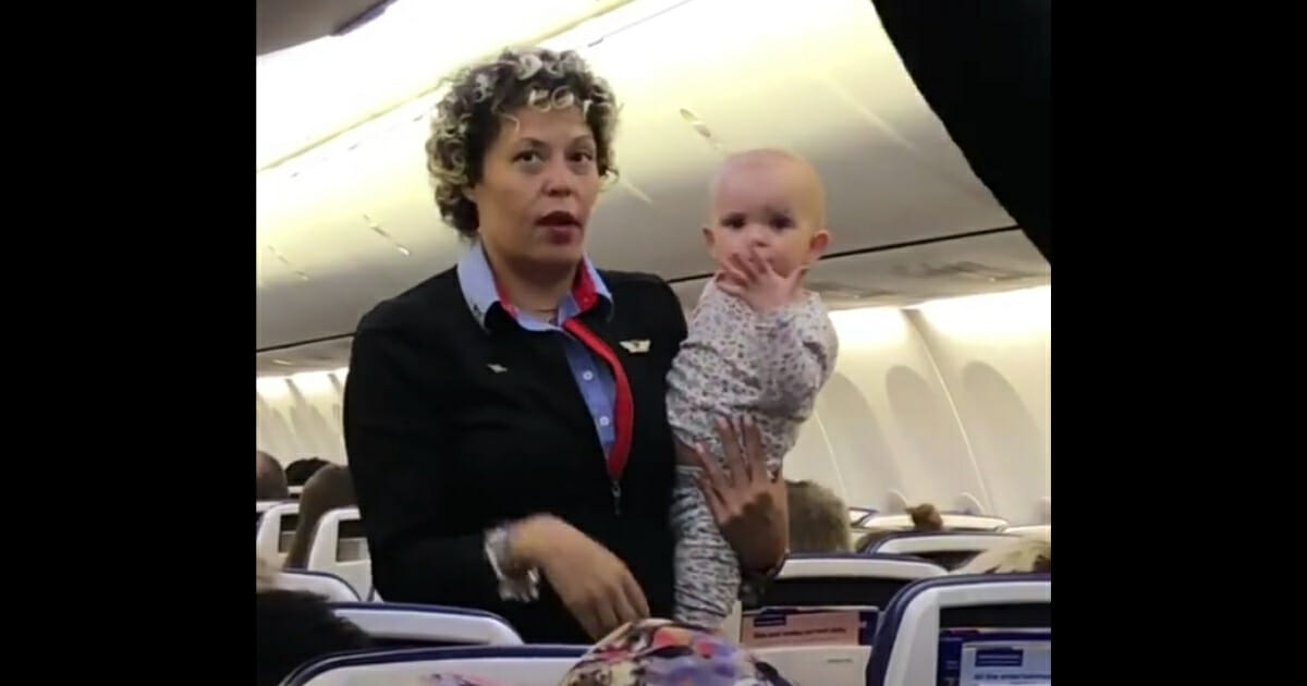 A flight attendant holds a baby on a plane.