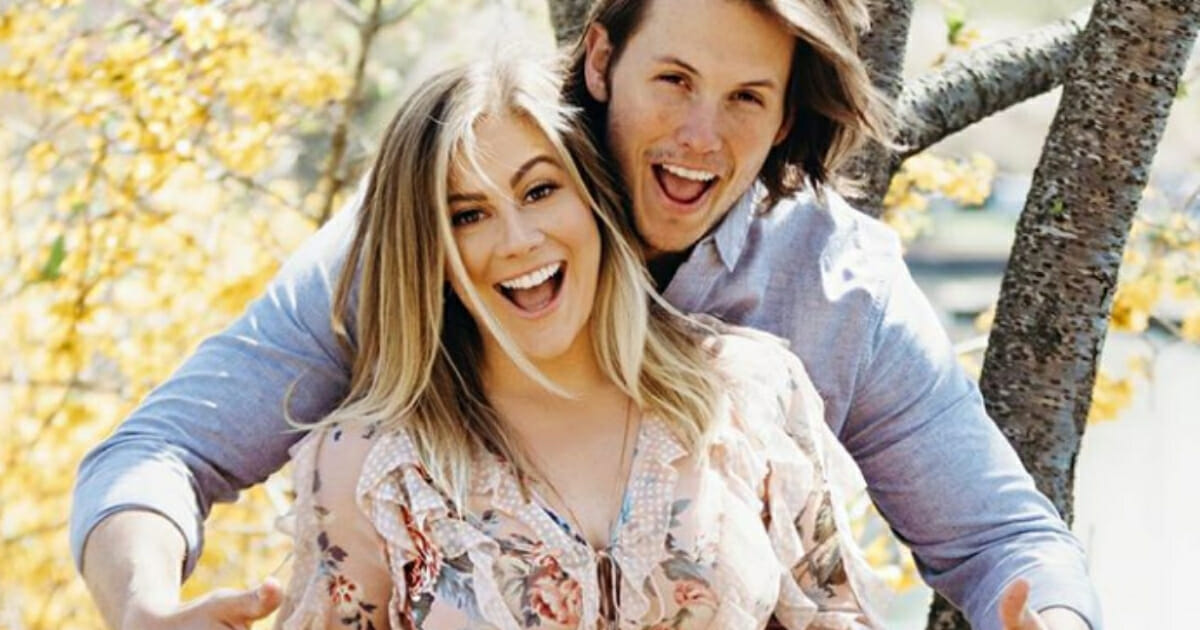 Andrew East points at Shawn Johnson's belly while both smile.
