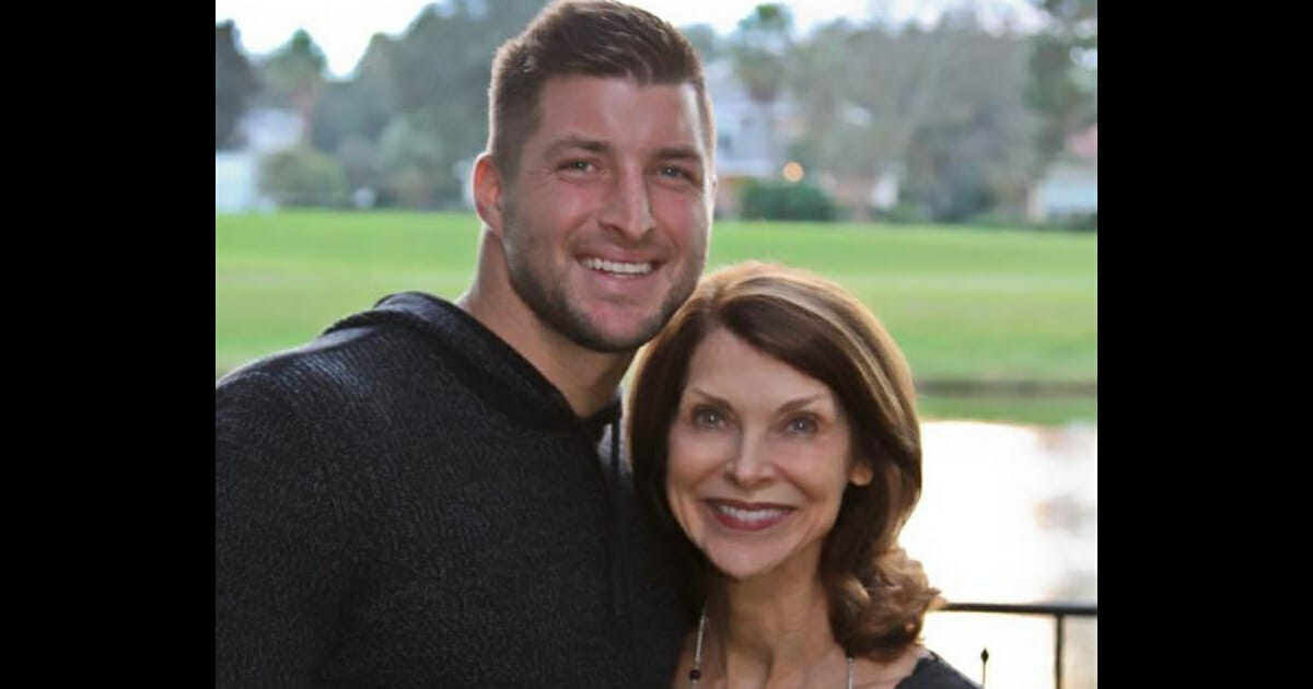 Tim Tebow standing next to his mother with his arm wrapped around her, both smiling.