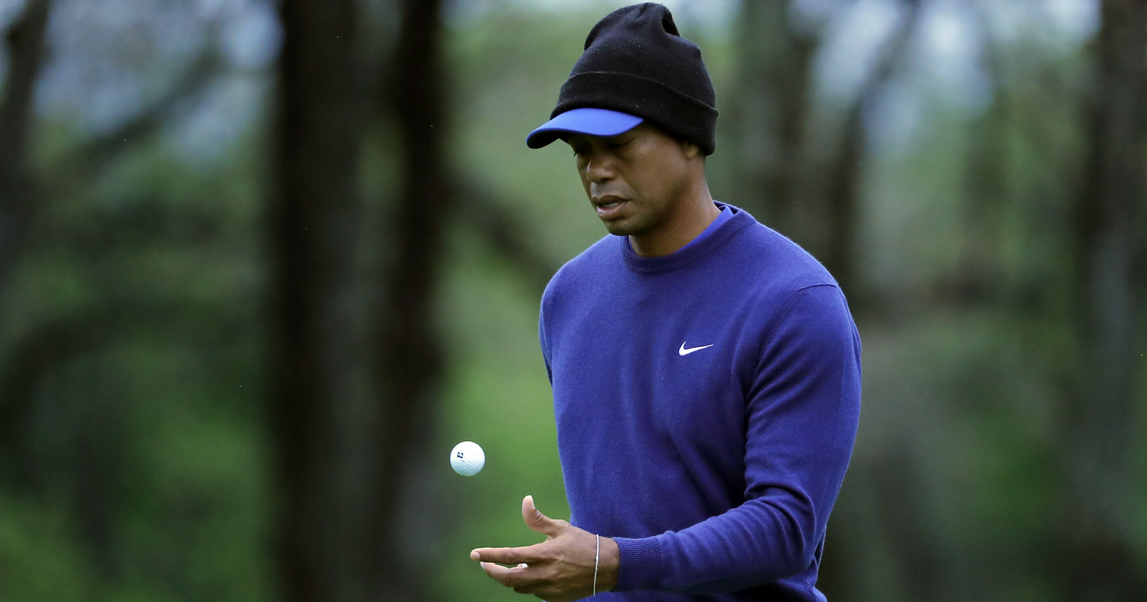 Tiger Woods, wearing cold weather gear, flips his ball.