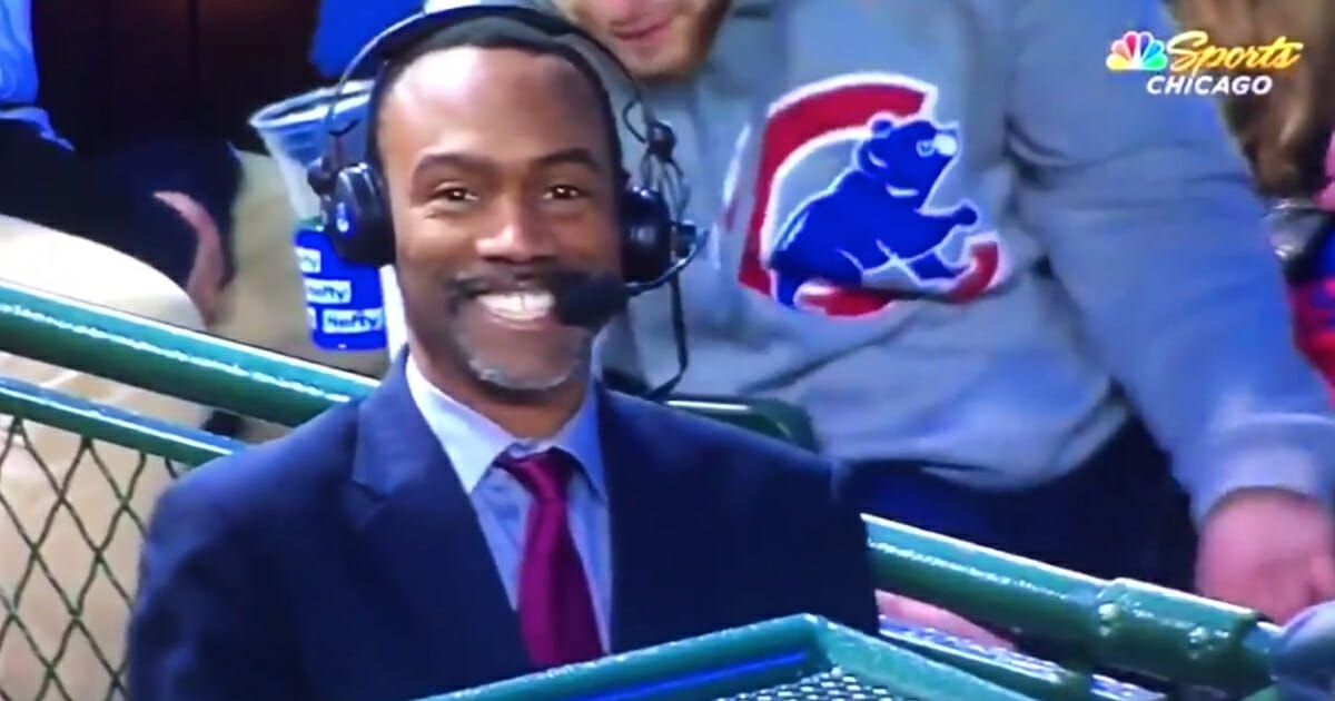A man in a Cubs sweater gestures behind NBC Sports Chicago analyst Doug Glanville.