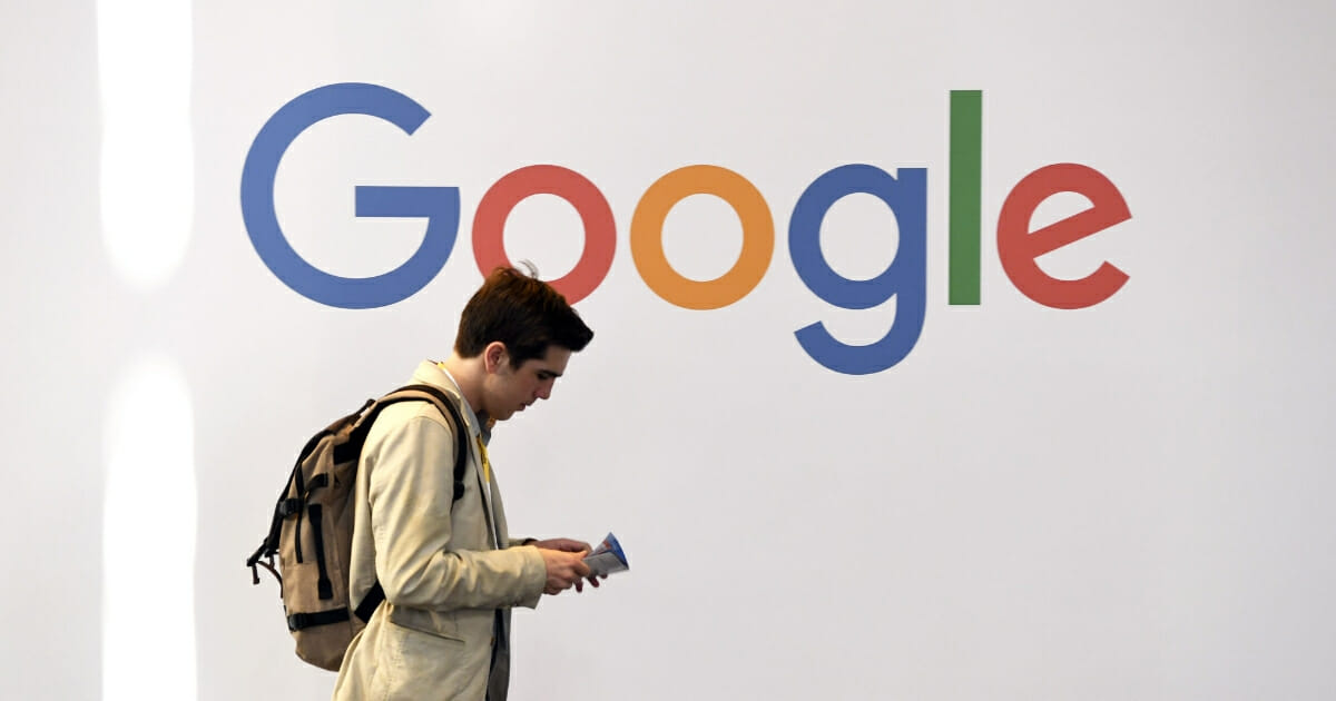 A man walks past the Google logo on a wall