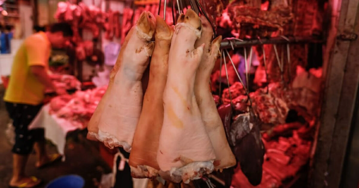Pig trotters hang from hooks as a butcher prepares pork meat at a market in Hong Kong on May 11, 2019. Hong Kong will cull 6,000 pigs after African swine fever was detected in an animal at a slaughterhouse close to the border with China.