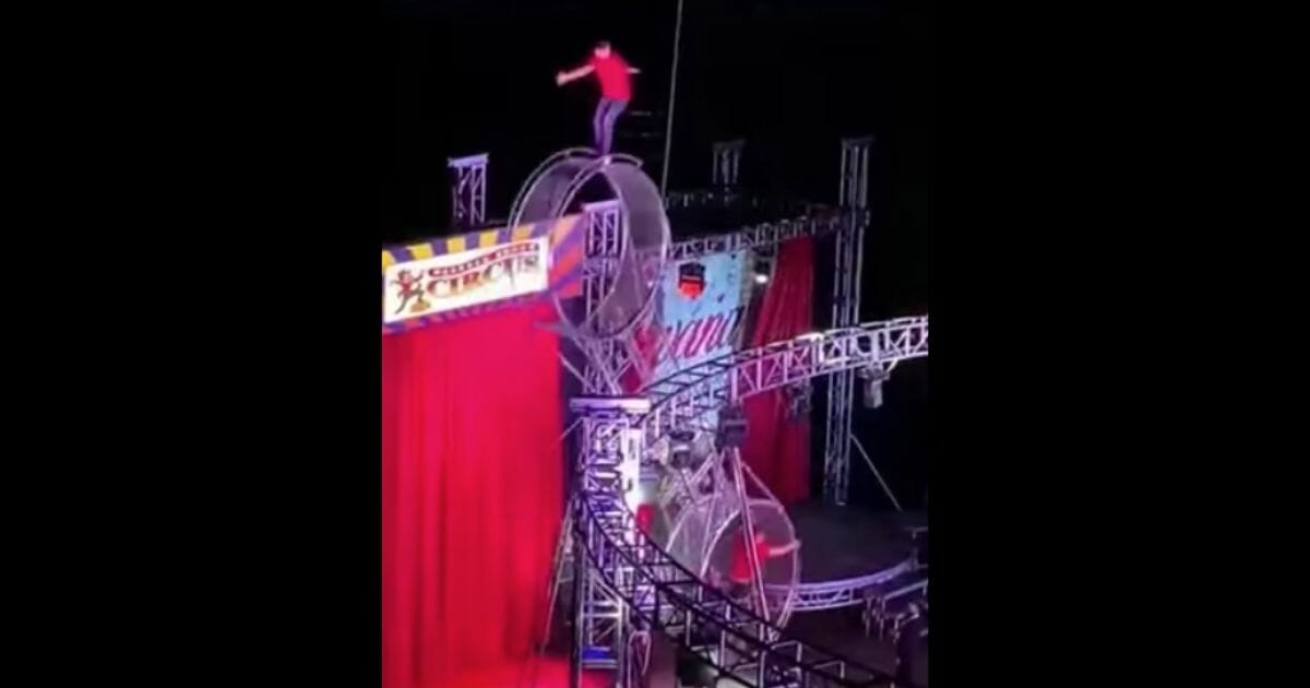 A circus performer stands on top of a spinning wheel