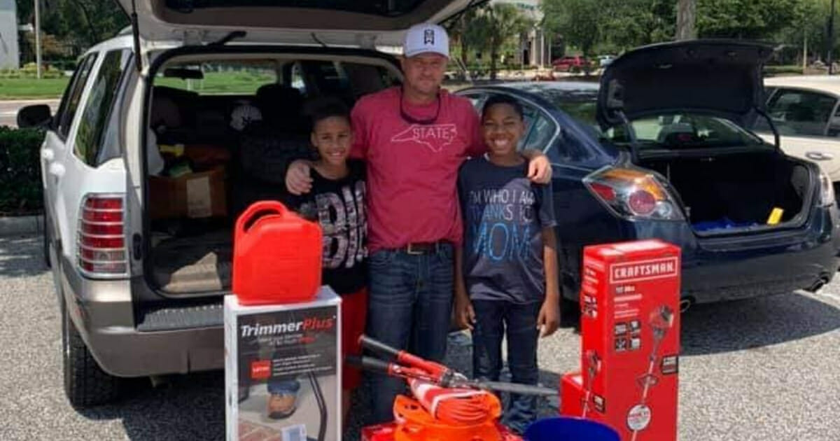 A man stands with two boys and lawn equipment.