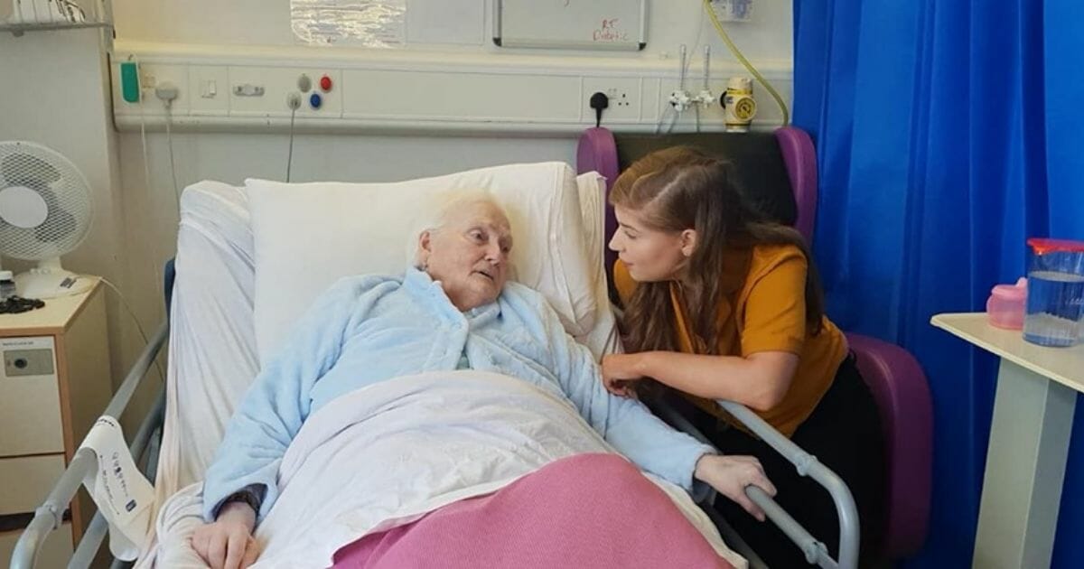 A young woman next to an elderly woman's hospital bed.