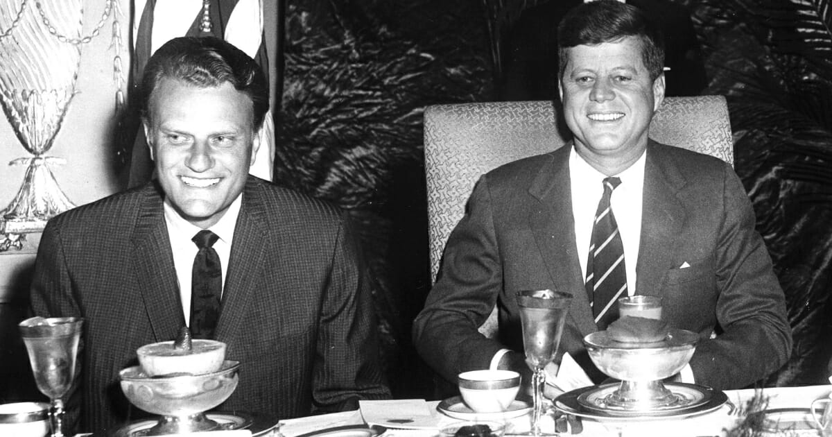 Christian evangelist Billy Graham, left, sits with former President John F. Kennedy, right. at the National Prayer Breakfast in Washington, D.C, on Feb. 9, 1994.