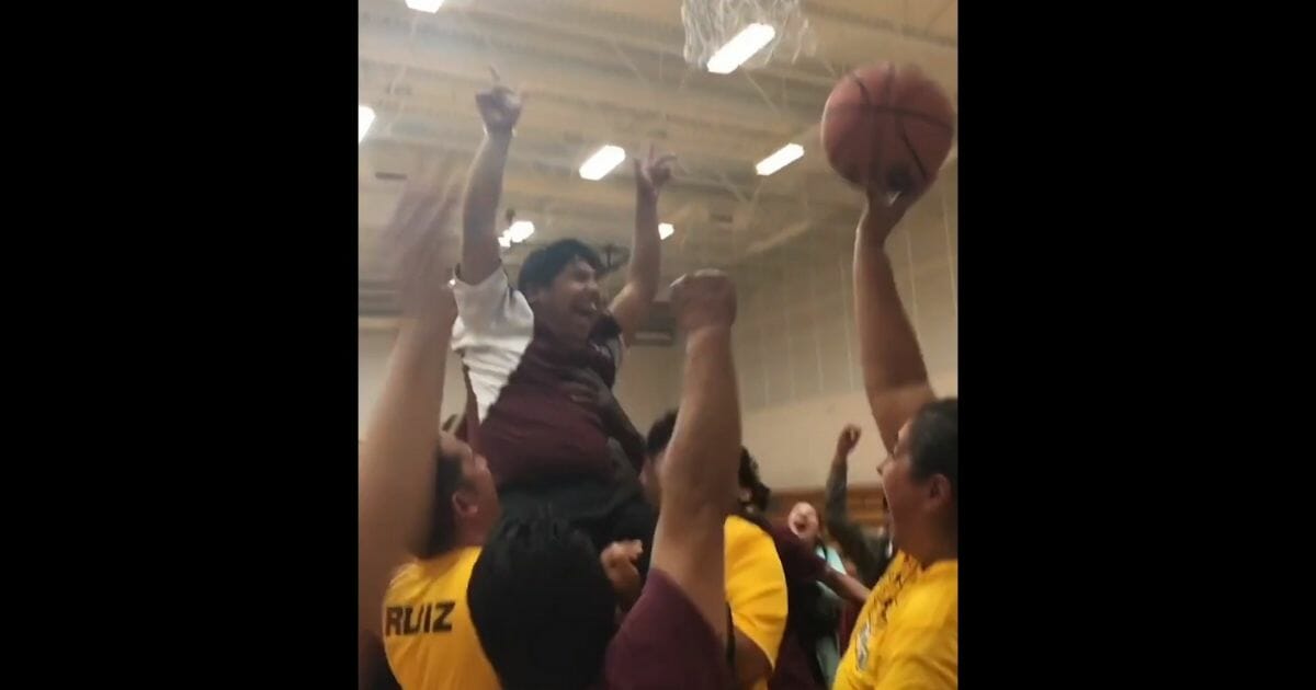 Student, held up by friends and coaches, throws his hands in the air after making a basket.