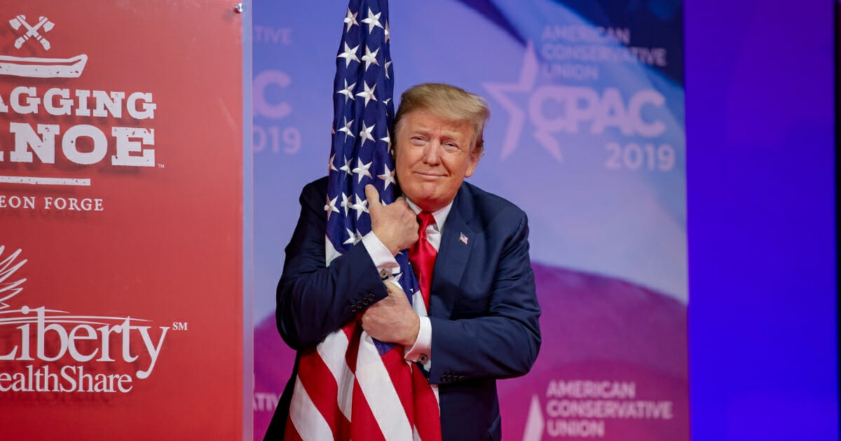President Donald Trump hugs the U.S. flag during CPAC 2019 on March 2, 2019 in National Harbor, Maryland.