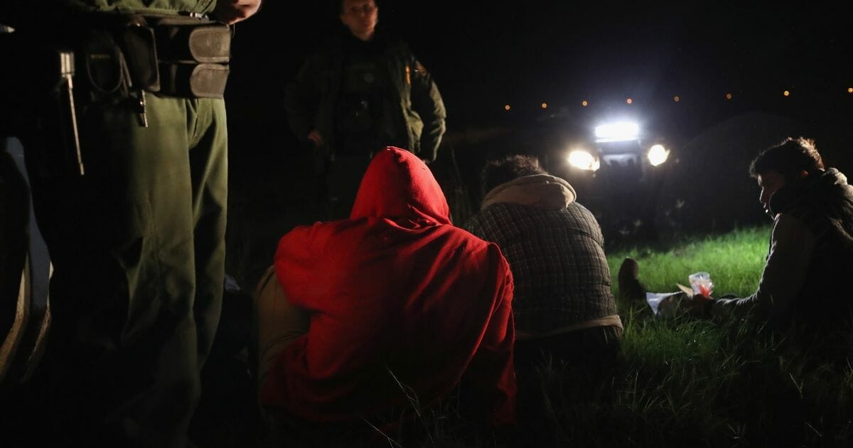 Three immigrants sitting on the ground after being apprehended.