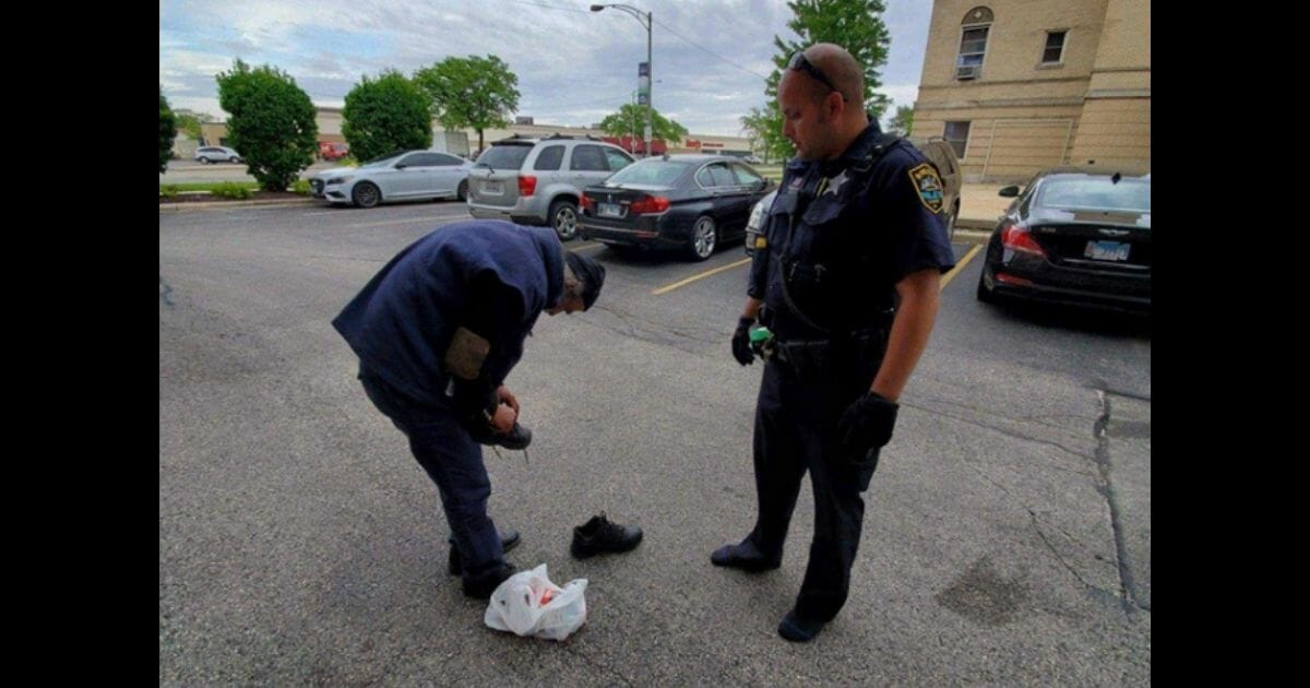The officer stands in his socks and watches as the homeless man tries on his shoes.