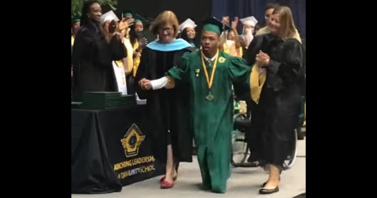 Jericho crosses the stage with the help of two teachers.