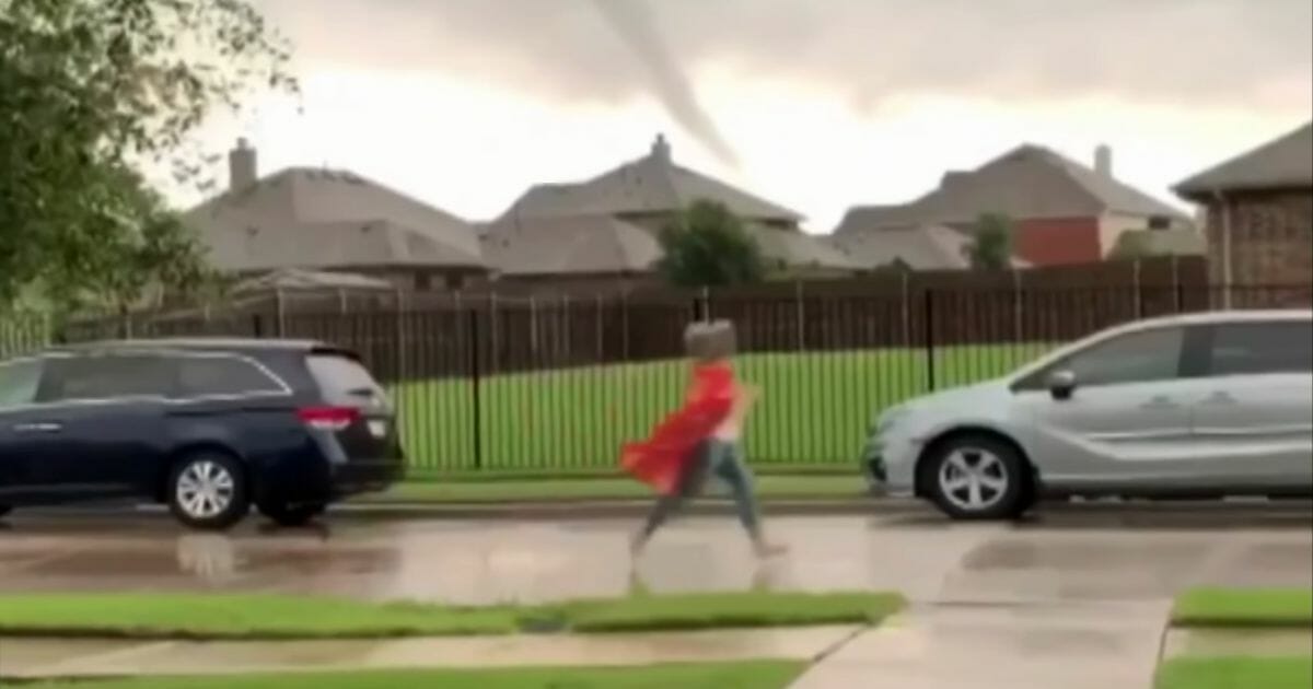 Teacher runs down line of parked cars with the tornado visible in the background.