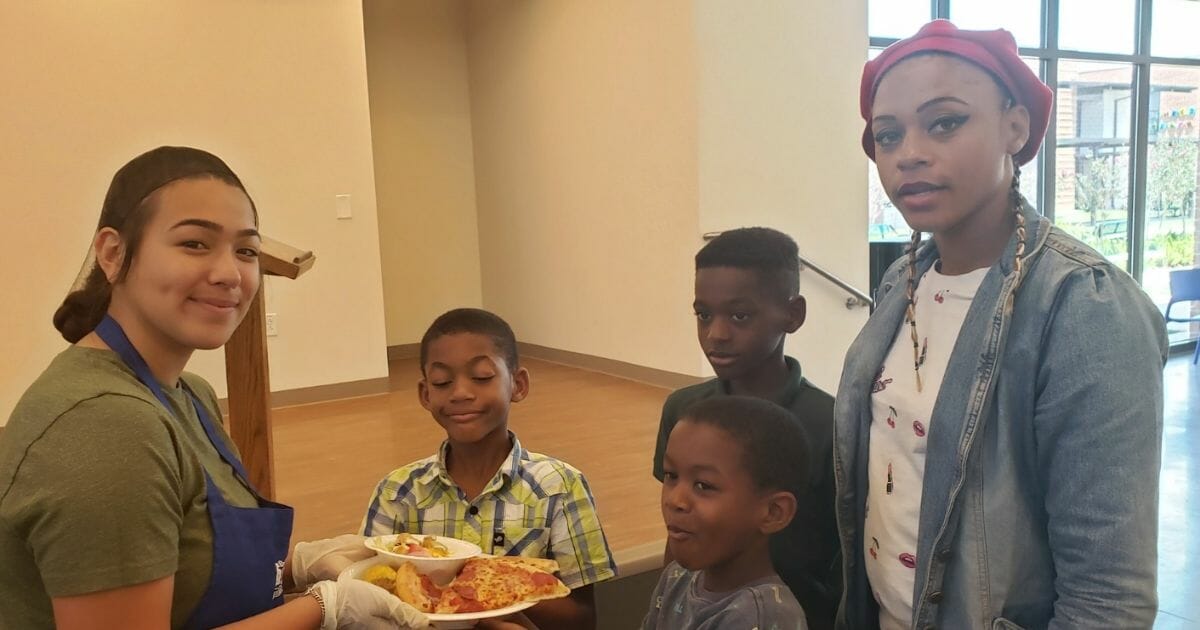 A teenager serves pizza to children.