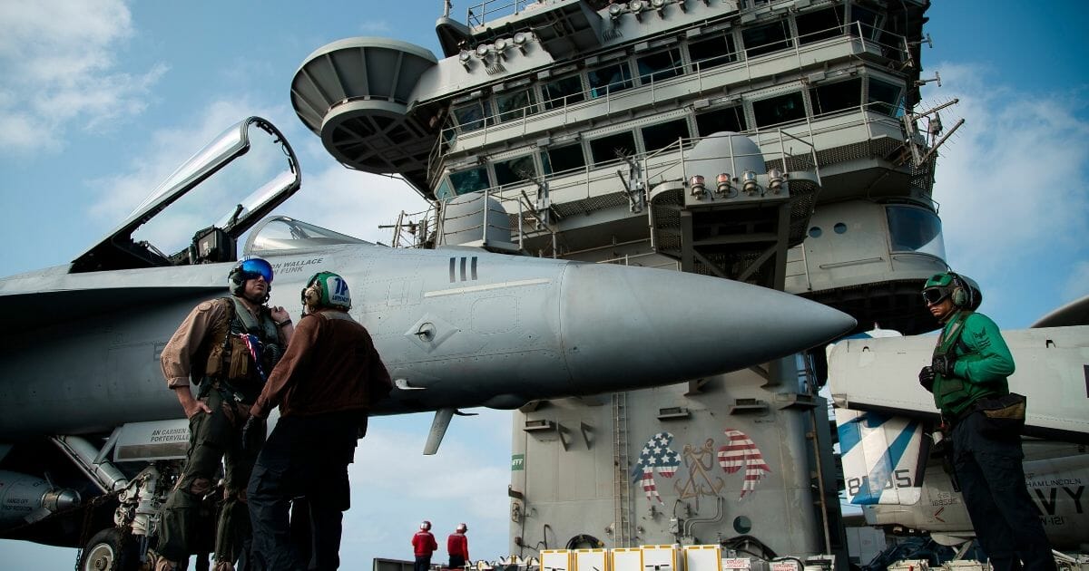 A Navy pilot talks with a crew member near a plane on the USS Abraham Lincoln.