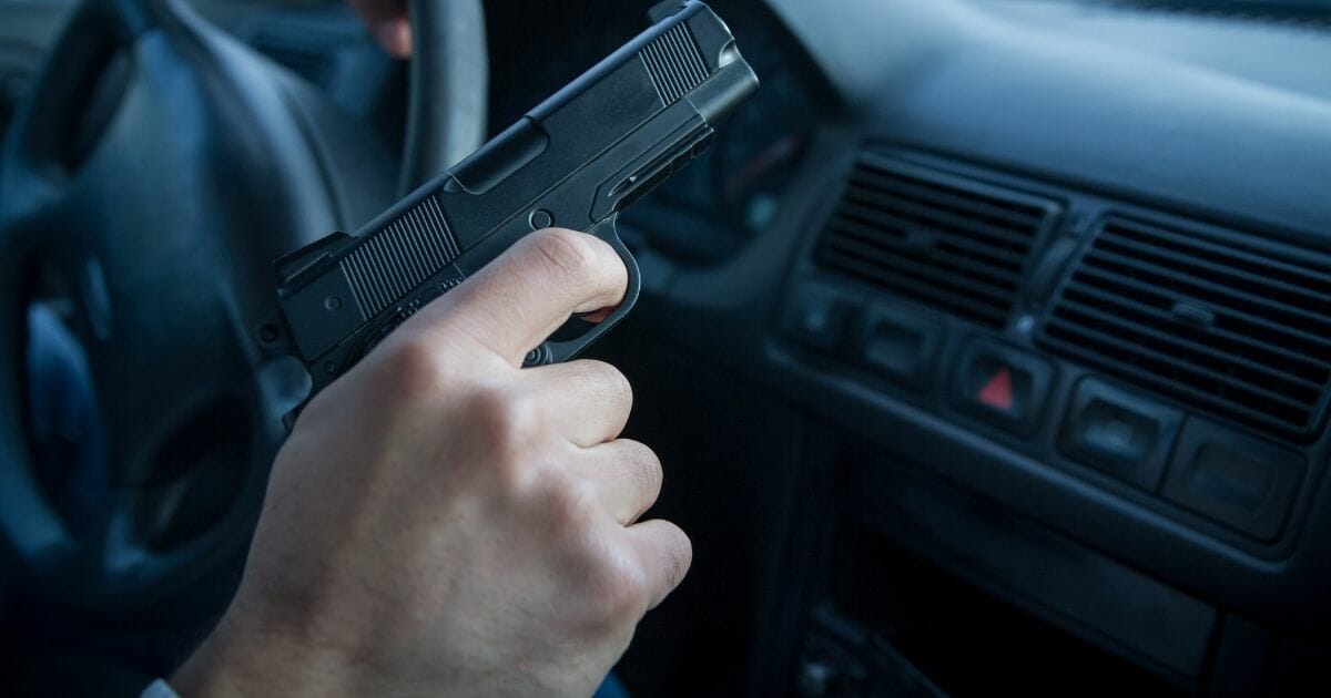 Man's hand holding gun in a car.