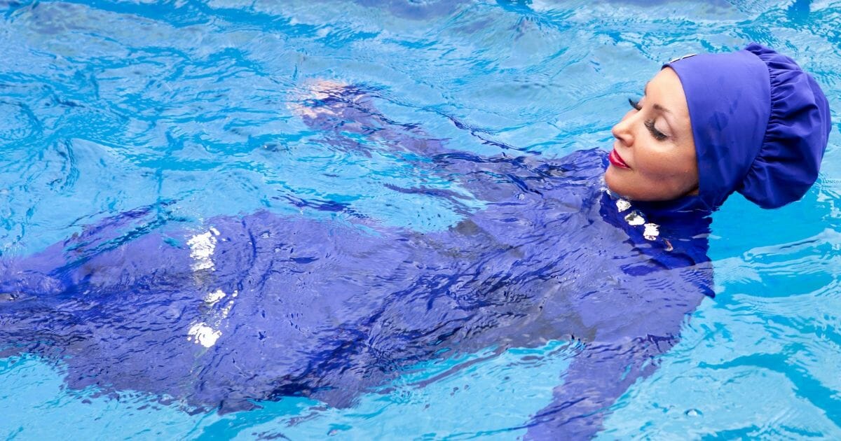 Woman in a pool wearing a burkini -- which leaves only her face and hands visible.