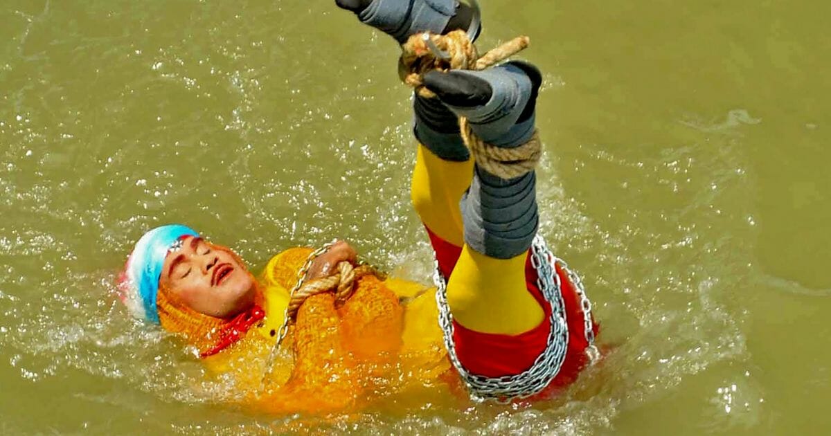Indian stuntman Chanchal Lahiri, known by his stage name "Jadugar Mandrake", is lowered into the Ganges river, while tied up with steel chains and ropes.