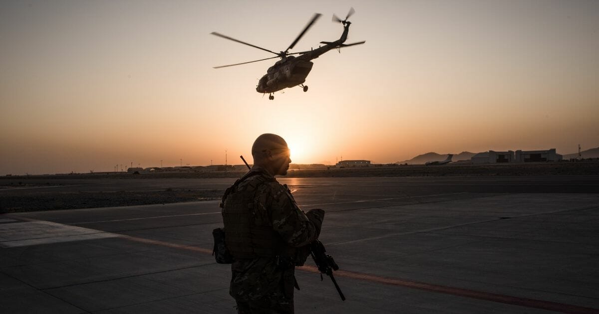 air force guard with gun, helicopter flying overhead, sunset