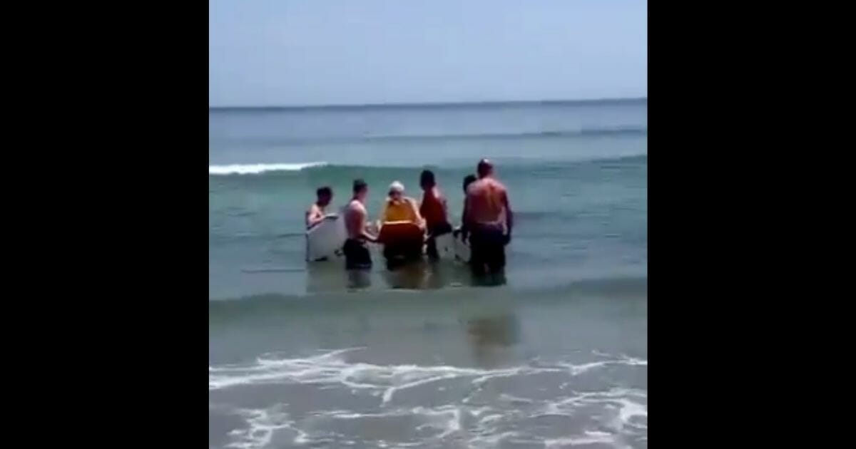Young men help an old man bodyboard