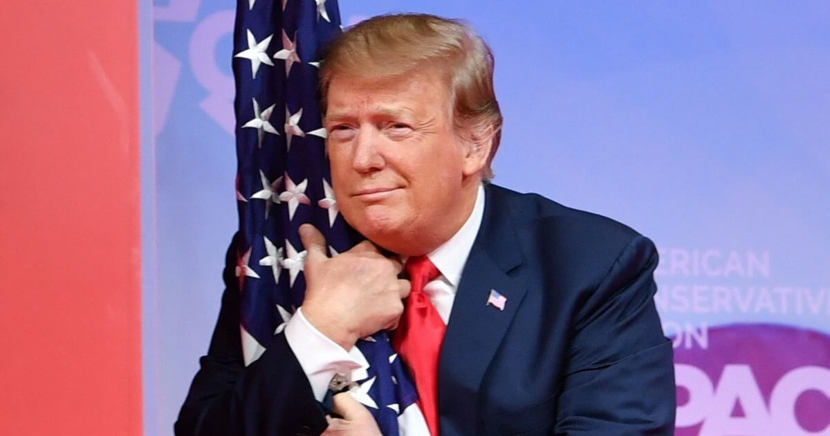 President Donald Trump hugs an American flag as he arrives to speak in National Harbor, Maryland, on March 2, 2019.