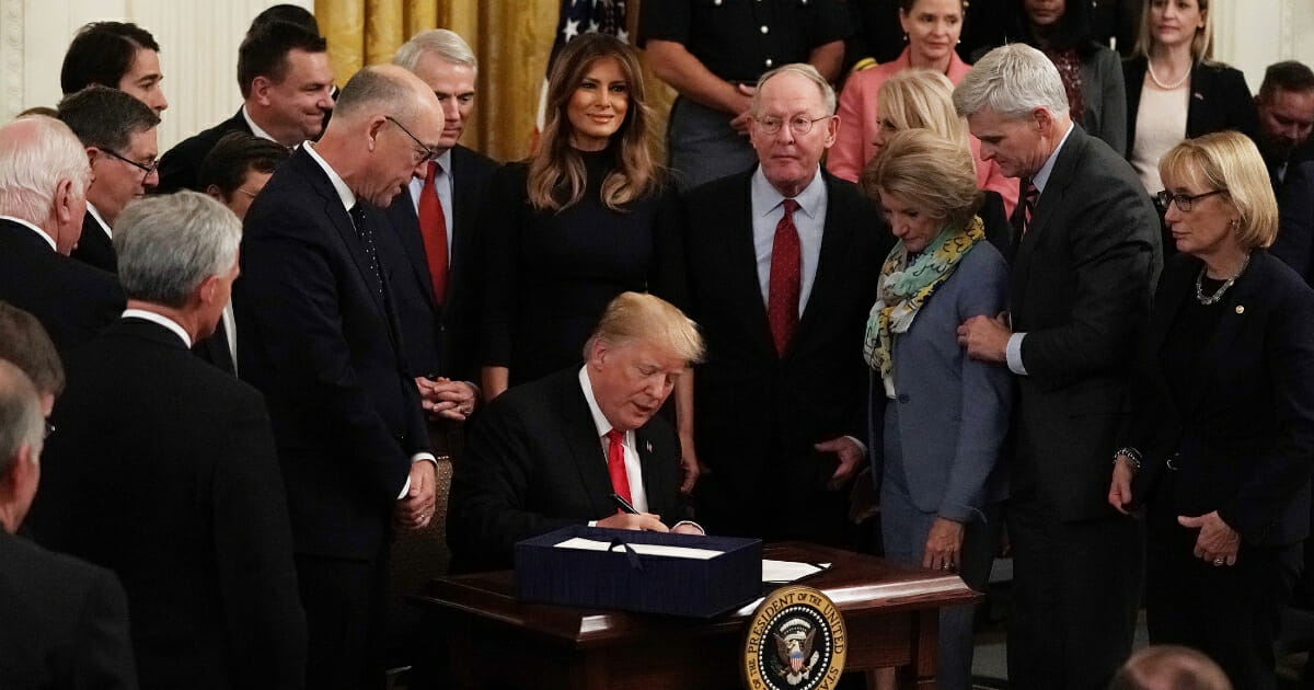 Flanked by lawmakers and first lady Melania Trump, President Donald Trump signs a bill to dedicate more resources to fight the opioid crisis during an Oct. 24, 2018, ceremony in the East Room of the White House.