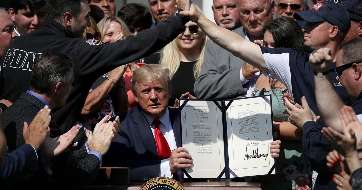 Surrounded by first responders and their families, President Donald Trump on Monday displays his signature on H.R. 1327, permanently funding the federal 9/11 victim compensation fund.
