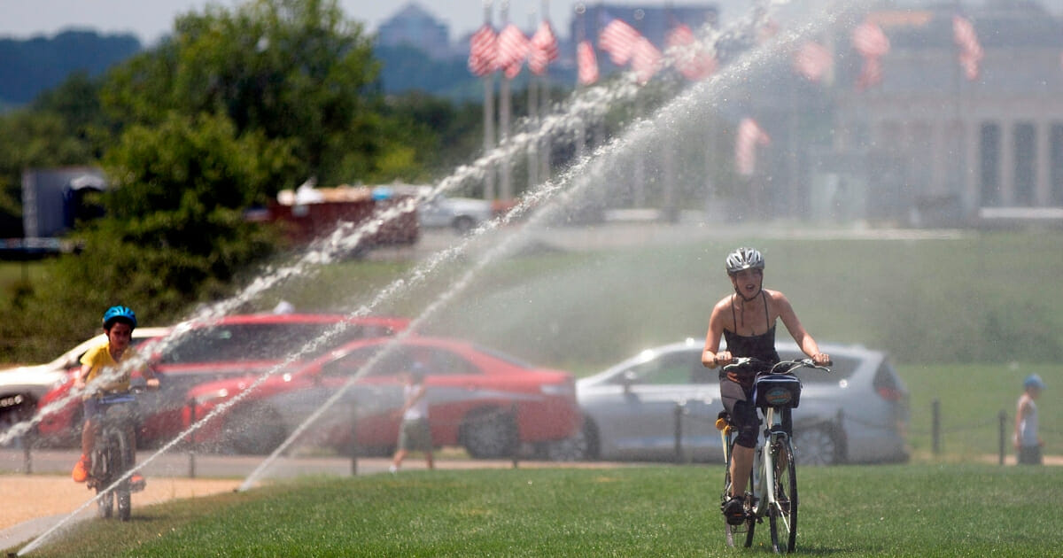 People ride their bicycles through sprinklers on the National Mall in Washington, D.C., on July 19, 2019.