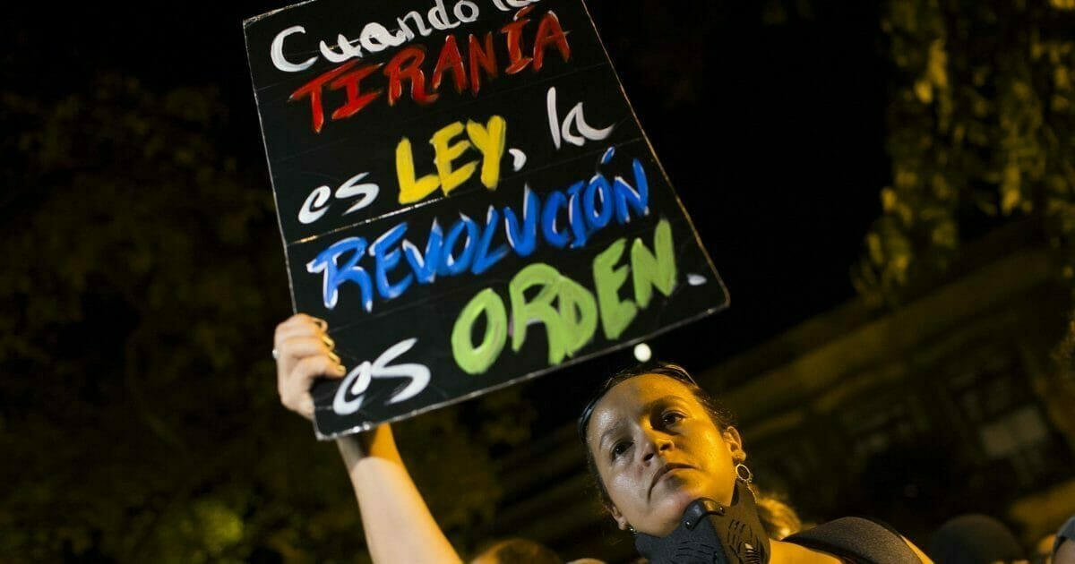 A woman holds a sign with message that reads in Spanish: "When tyranny is the law, a revolution is in order" during a protest outside the governor’s residence, the Fortaleza, after Pedro Pierluisi was sworn in as Puerto Rico's governor, in San Juan, Puerto Rico, Friday, Aug. 2, 2019.