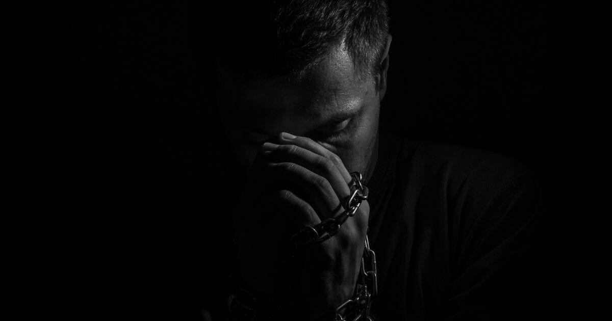 Male prisoner praying with his hands shackled in chains.