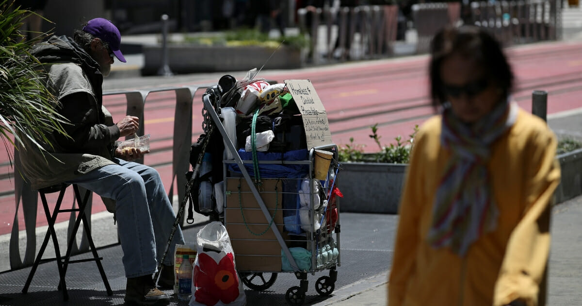 A pedestrian walks by a homeless man who is begging for money on May 17, 2019, in San Francisco, California.