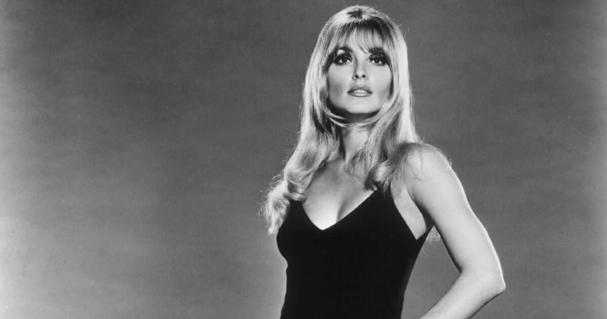 Studio portait of American actor Sharon Tate (1943 - 1969) posing in a black grown with her hand on her hip.