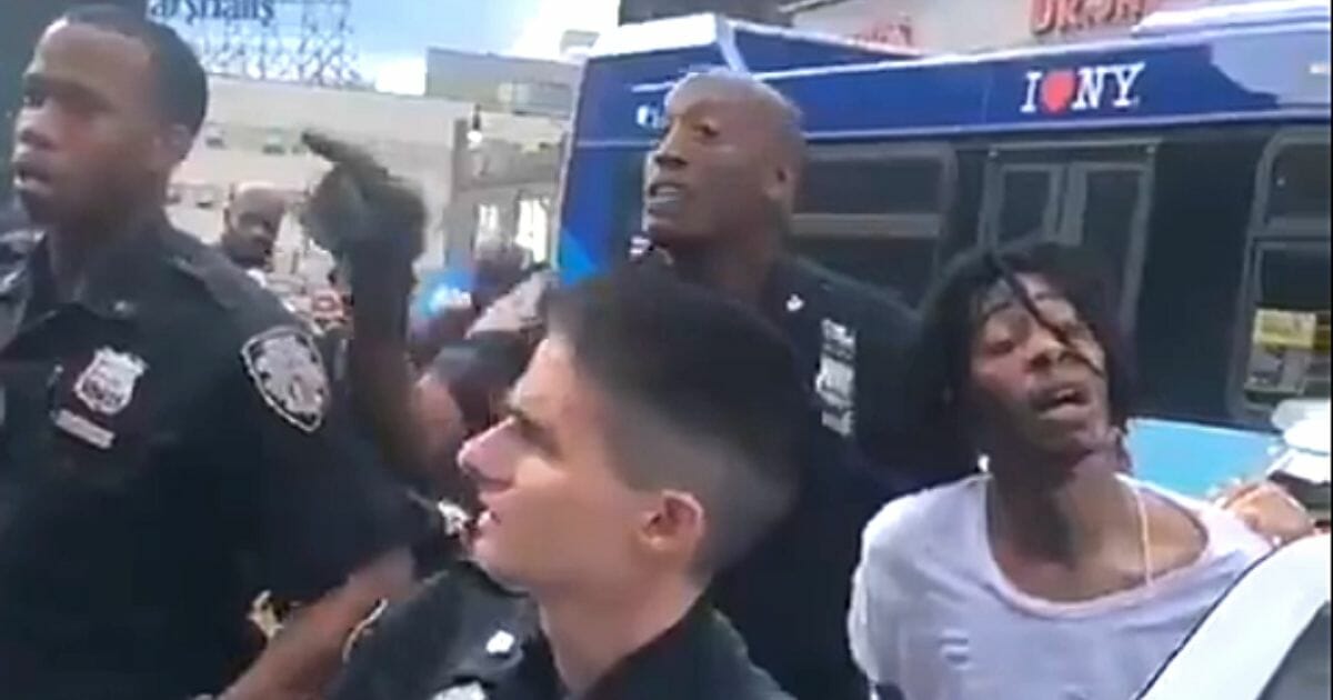 NYPD officers struggle to control a crowd and arrest a suspect.
