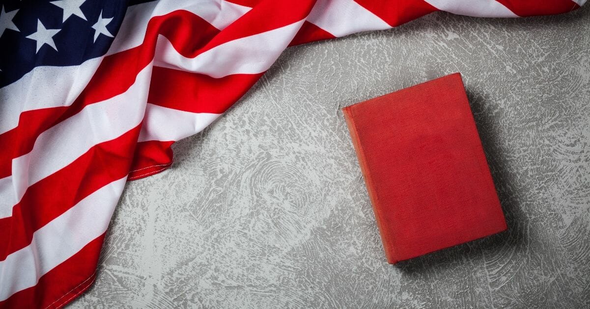 A red book sits on a table near an American flag.