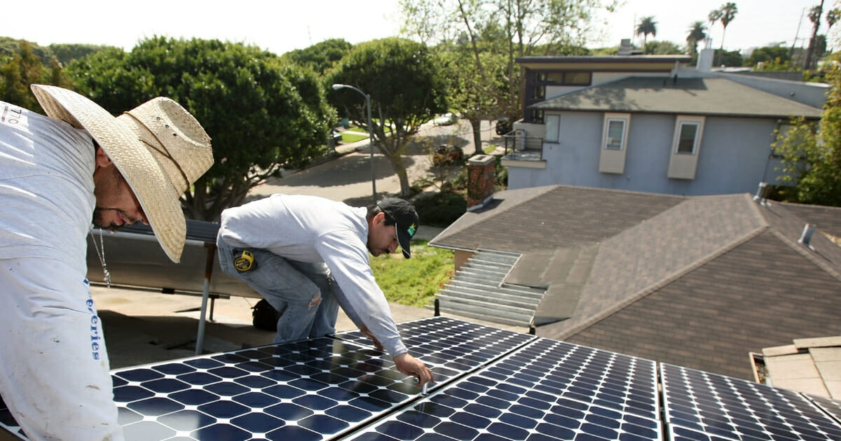 Worker install solar electric panels on a residential rooftop in Santa Monica, California.