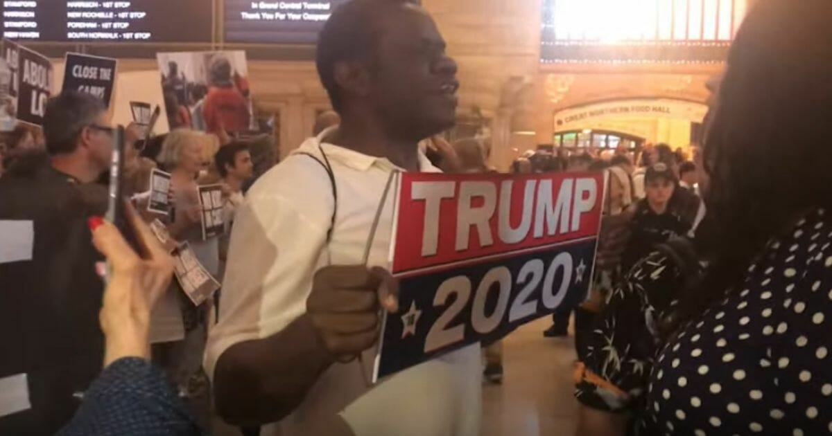 A man holds a pro-Trump sign at an anti-ICE rally.