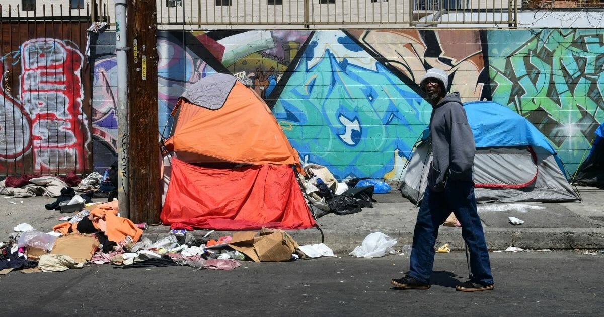 A pedestrian walks past tents and trash on a sidewalk in downtown Los Angeles on May 30, 2019.