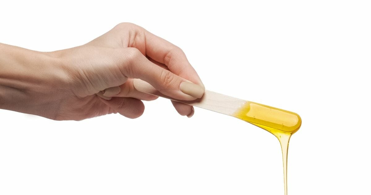 Stock image of a hand holding beauty wax on a wooden spatula.