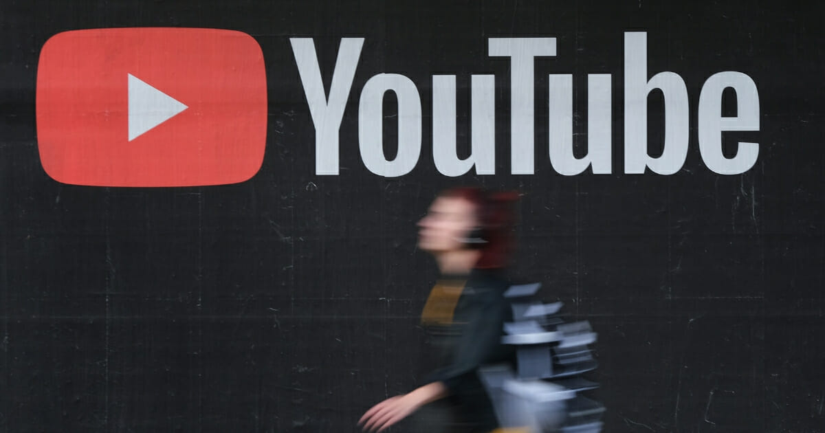 A young woman wearing headphones walks past a billboard advertisement for YouTube on Sept. 27, 2019, in Berlin, Germany.