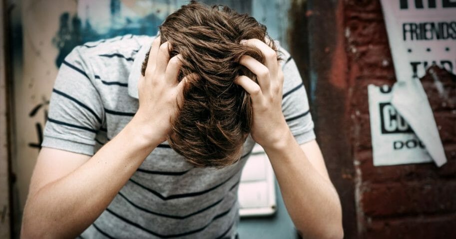 Emotionally depressed young male is sitting on the floor with his hands on his head.