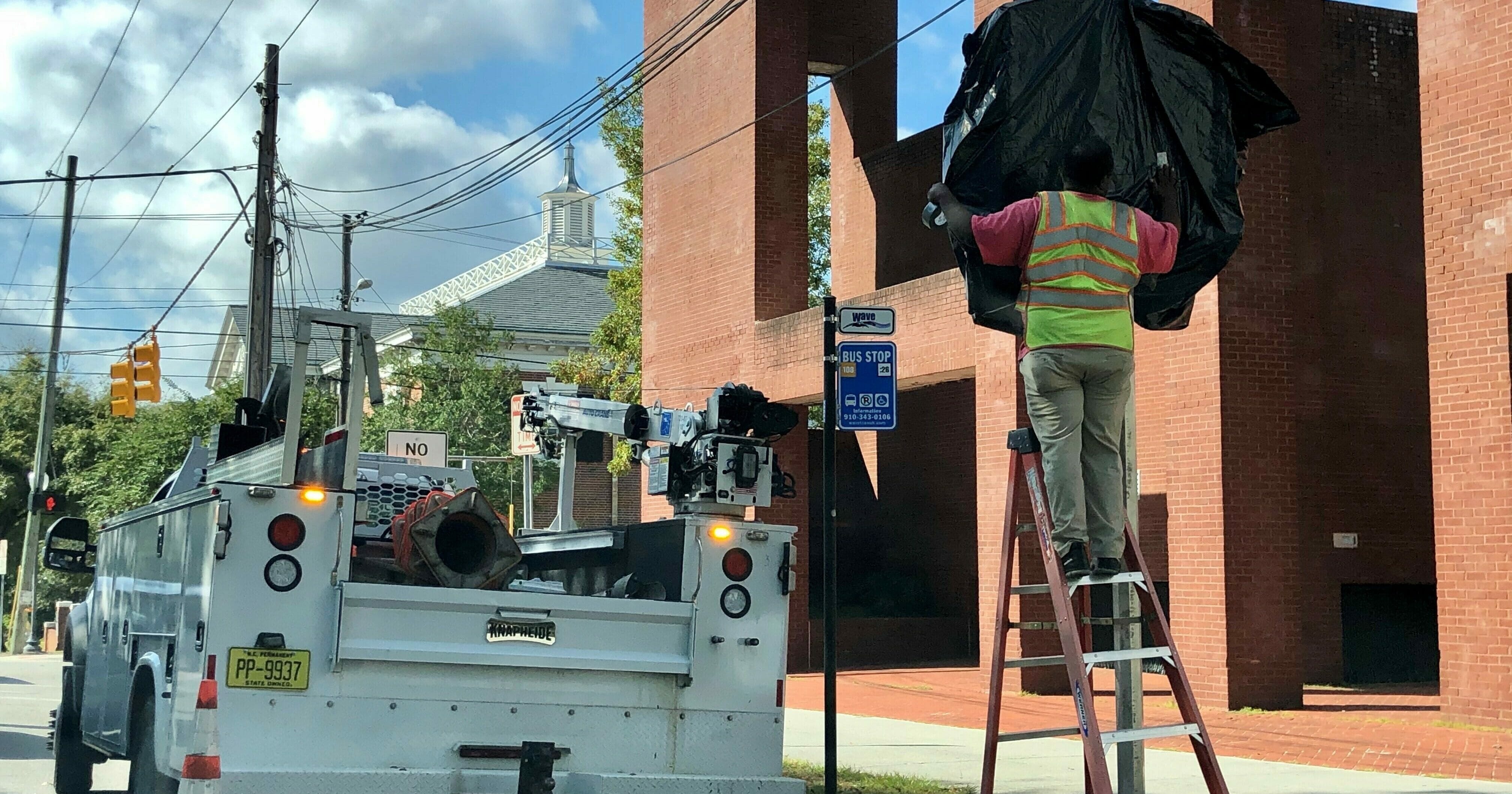 In this Oct. 28, 2019, photo, a worker with the North Carolina Department of Transportation covers the 1898 Wilmington coup highway historic marker that will be unveiled at a ceremony in Wilmington, North Carolina. The marker commemorates the violent overthrow by white Democrats of the fusion government of legitimately elected blacks and white Republicans in Wilmington. The Democrats burned and killed their way to power in what's viewed as a flashpoint for the Jim Crow era of segregation and the only successful coup d'etat in American history.