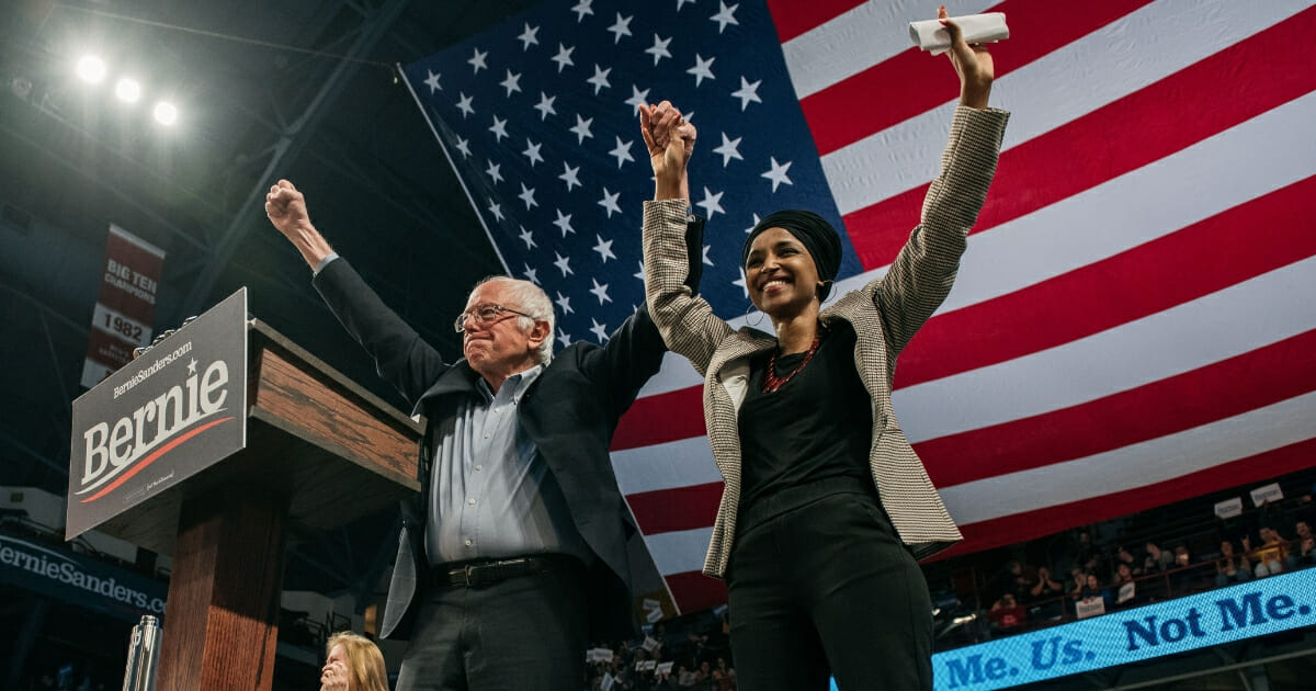 Democratic presidential candidate Sen. Bernie Sanders of Vermont holds hands with Rep. Ilhan Omar of Minnesota during a campaign rally at the University of Minnesota's Williams Arena.