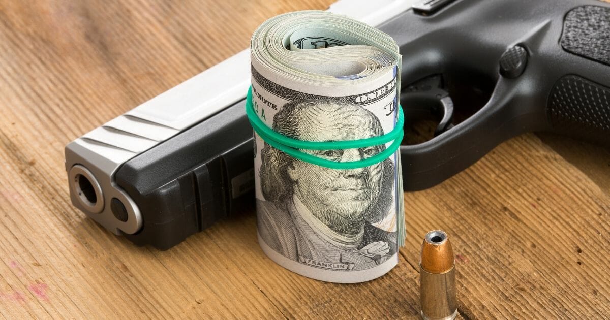 Handgun with a roll of 100 dollar bills and a single bullet lying on a wooden surface.