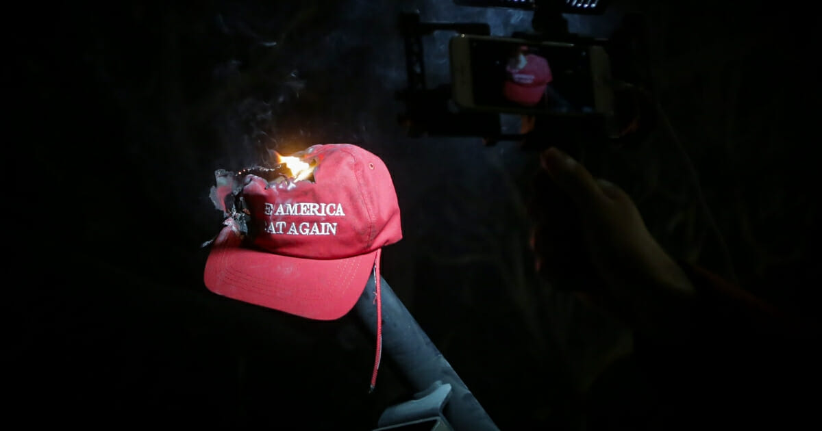 A Florida man has been charged with battery after allegedly spitting on a Trump supporter and slapping the MAGA hat off of his head. The image above shows a MAGA hat being burned.