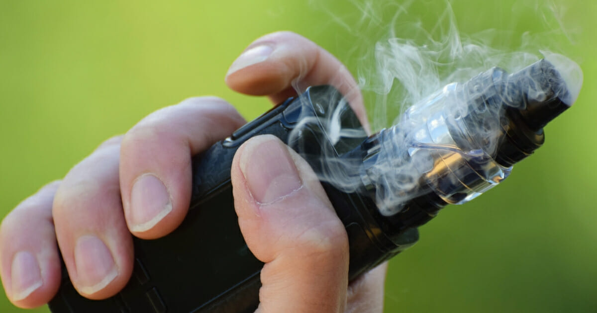 A man who is vaping holds his e-cigarette.
