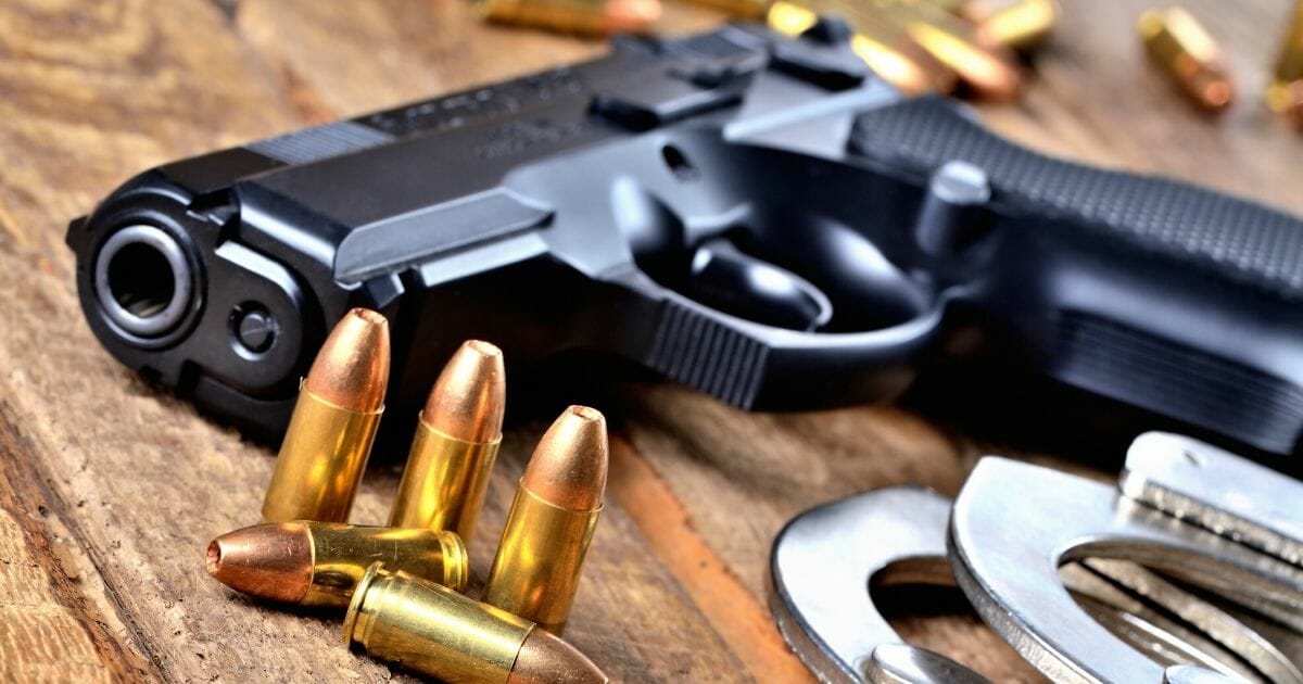 A 9 mm pistol handgun, special police hollow-point expanding bullets and handcuffs on a wooden table.