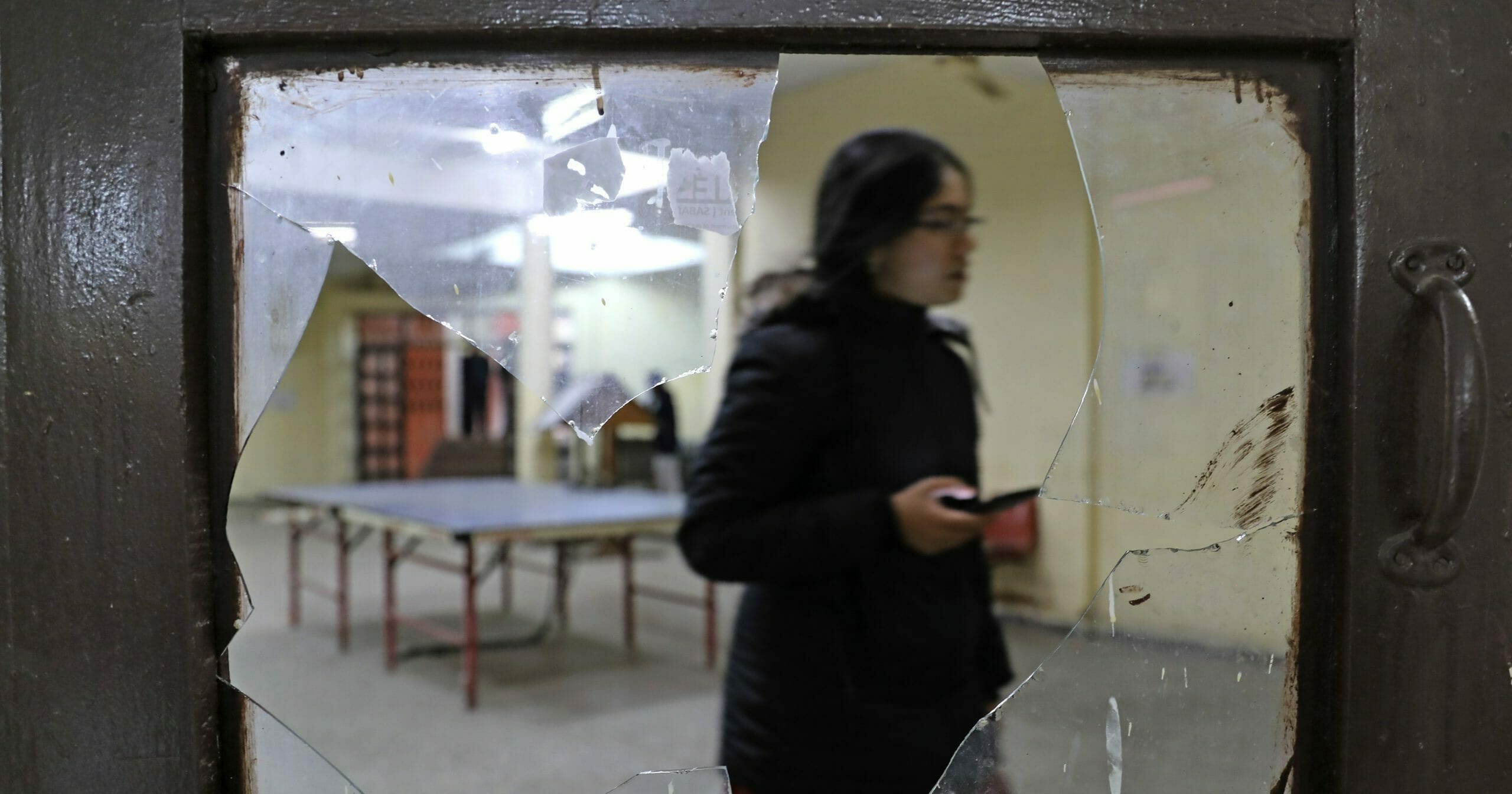 A student is seen through broken glass as she walks inside the hostel canteen room vandalized after Sunday's assault by masked assailants at the Jawaharlal Nehru University in New Delhi, India, on Jan. 6, 2020.