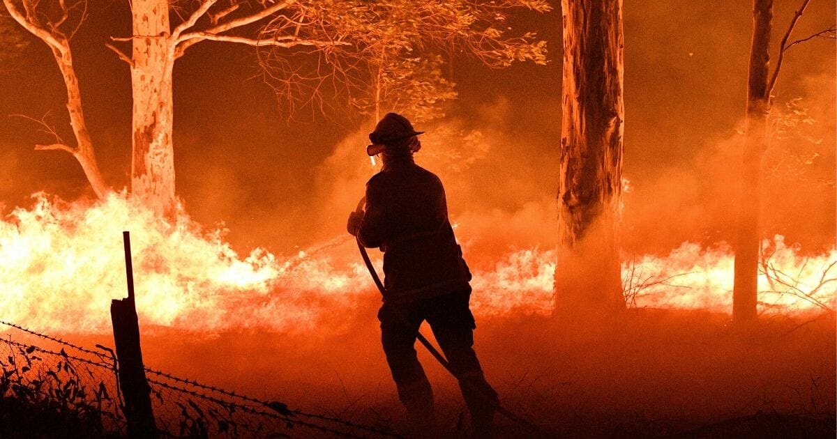 A firefighter hoses down trees and flying embers Dec. 31, 2019, in an effort to secure nearby houses from bushfires near the town of Nowra in the Australian state of New South Wales.