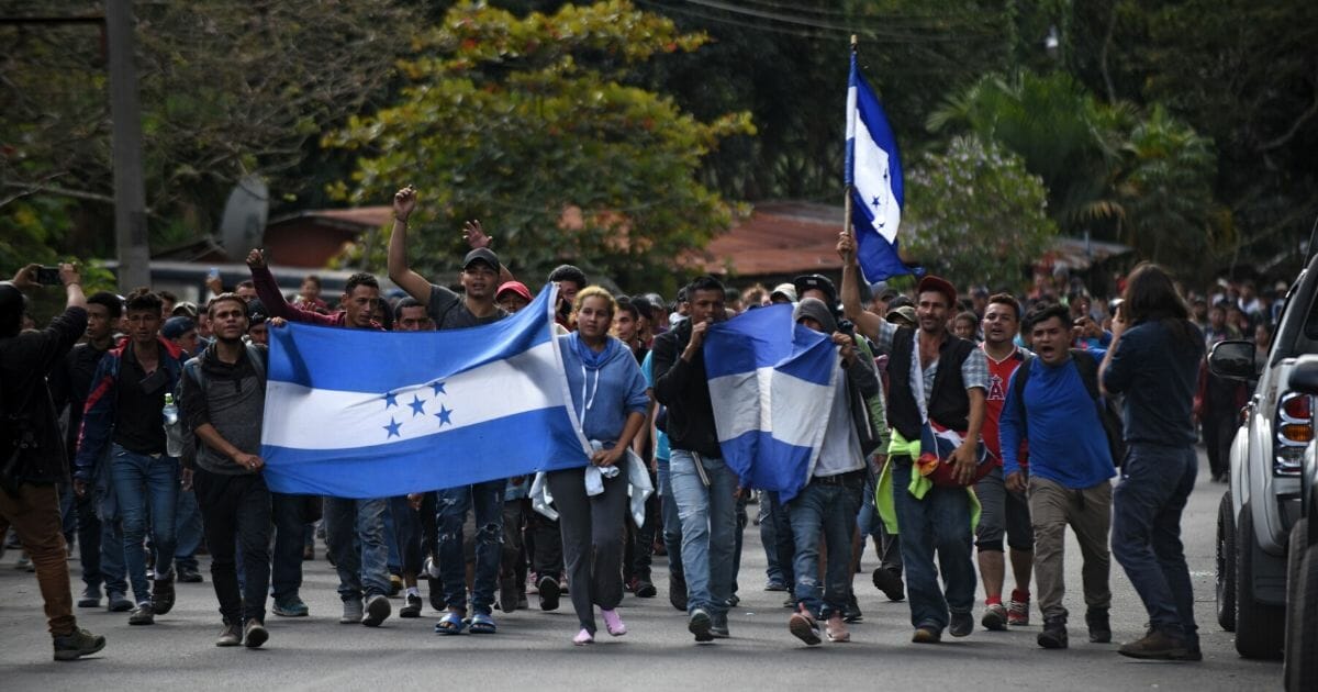 Honduran migrants walk with national flags after going through a police fence at the Agua Caliente border crossing from Honduras, near Esquipulas, Chiquimula department, Guatemala, on Jan. 16, 2020, on their way to the US.